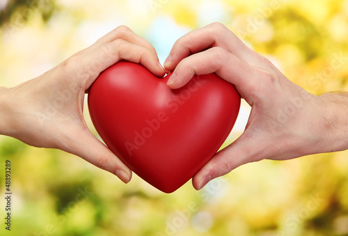 Red heart in woman and man hands  on green background