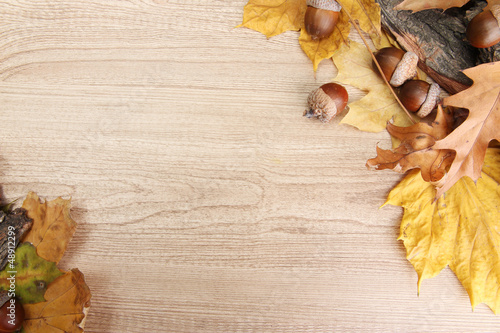 brown acorns on autumn leaves, on wooden background
