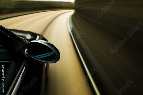 Side view of black car driving in country road.