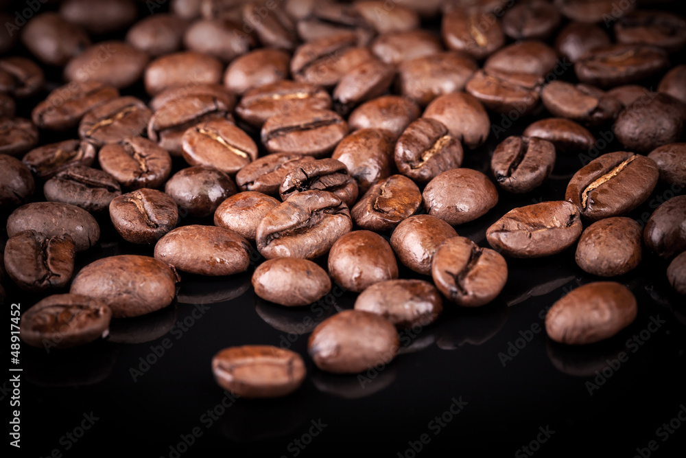Naklejka premium Fresh roasted coffee beans on black shine table. Closeup photo