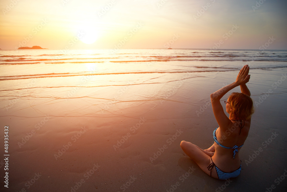 Woman meditating on the beach at sunset.