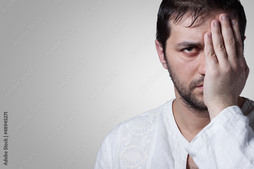 Young bearded man with his hand covering an eye Young bearded man with his hand covering an eye