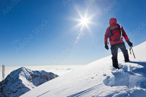 Mountaineer reaches the top of a snowy mountain in a sunny winte