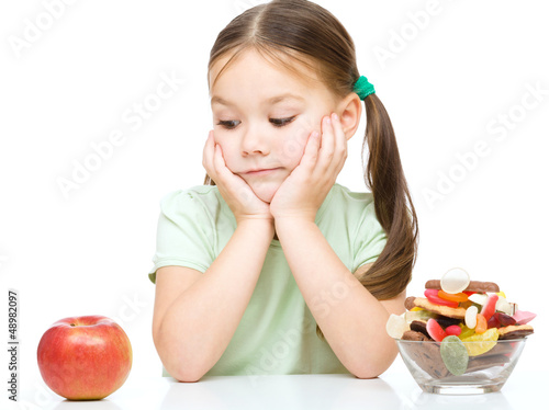 Little girl choosing between apples and sweets