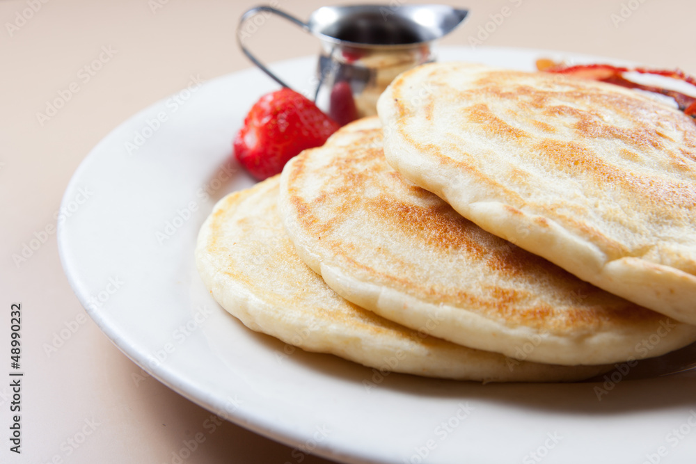 side view of stack of pancakes with bacon and syrup