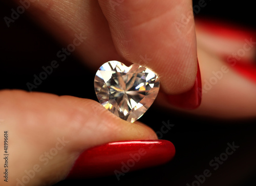 Fingers with red nails holding heart shaped white diamond
