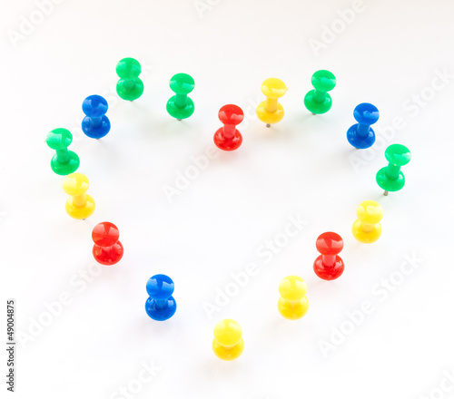 Multi color thumb-tacks arranged in heart shape on white.