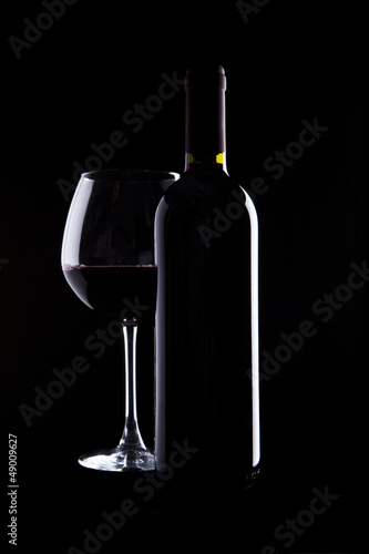elegant glass and bottle of red wine on black background