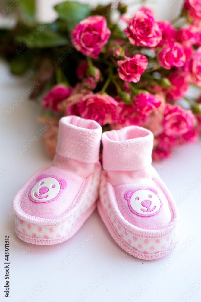 Baby girl shoes and pink roses on a table. new born girl shoes . Baby girl shoes and pink roses on a table. new born girl shoes .
