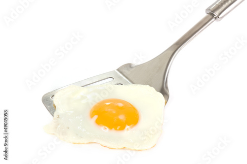 Fried egg on a silver spatula over white