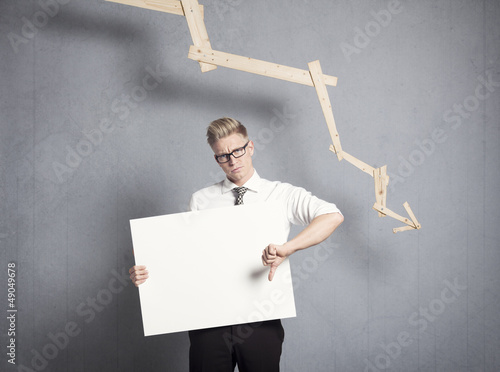 Fotografering Unhappy businessman showing panel in front of descending graph.