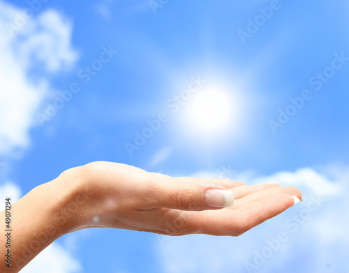 Sun on human hand against blue sky.