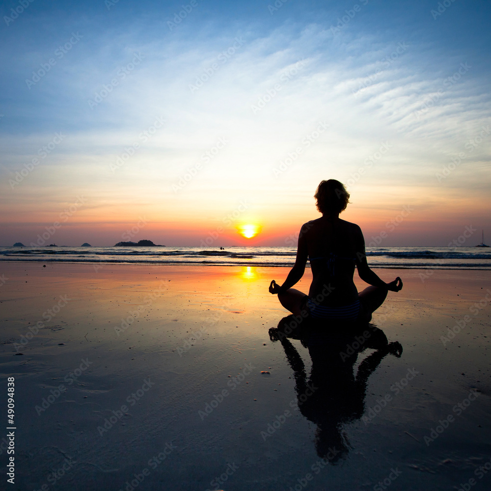 Silhouette yoga woman sitting on sea coast at sunset.