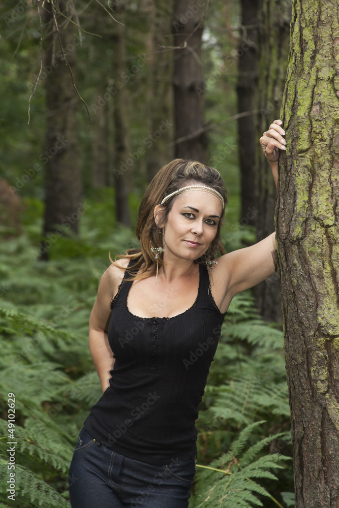 attractive woman standing in woodland leaning against a tree attractive woman standing in woodland leaning against a tree