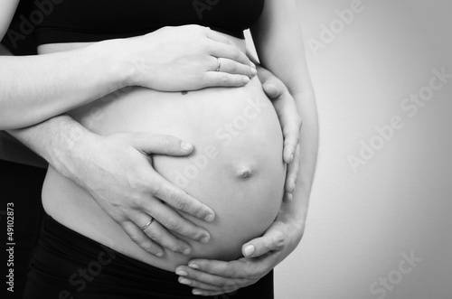 close-up of a pregnant belly with parents hands in black and whi