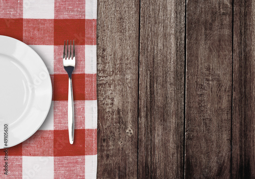 white plate and fork on old wooden table with red checked tablec