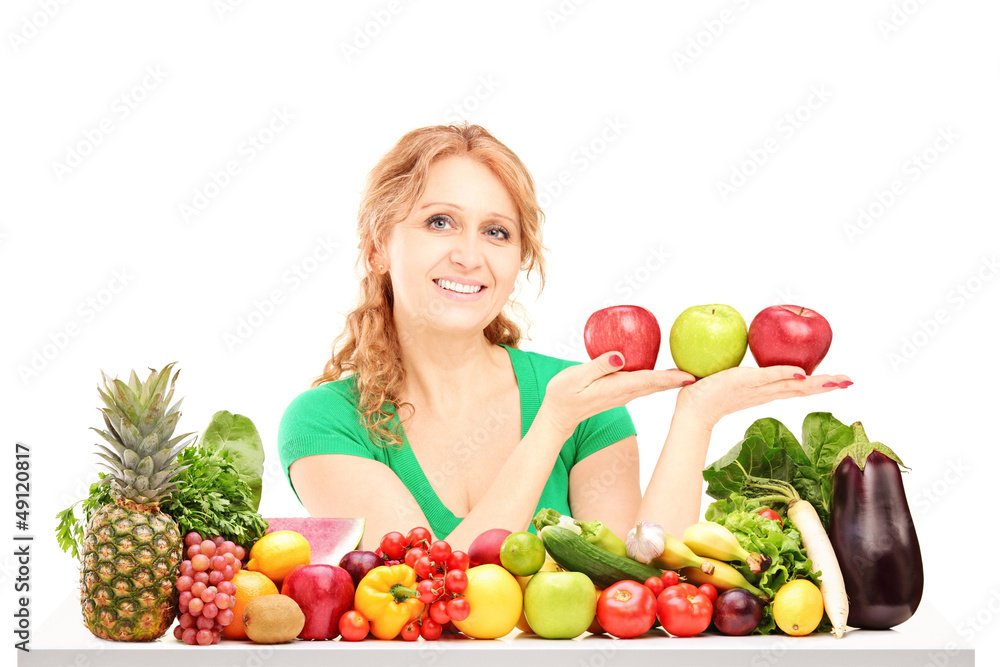 Woman sitting behind a table full of fruit and vegetable and hol Woman sitting behind a table full of fruit and vegetable and hol