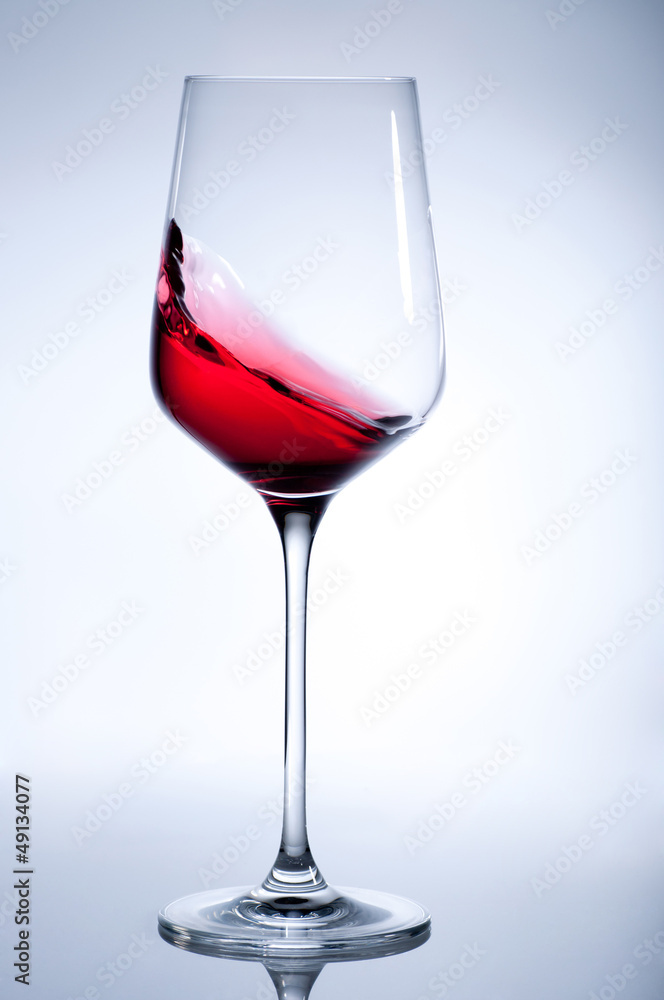 Red wine splashing in the elegant glass on gray Red wine splashing in the elegant glass on gray
