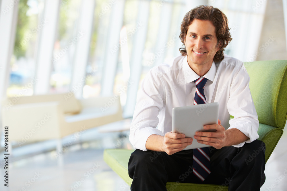 Businessman Sitting On Sofa In Office Using Digital Tablet Businessman Sitting On Sofa In Office Using Digital Tablet