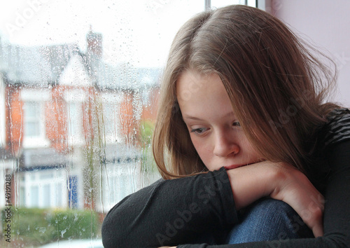 A young girl sad on her window close to tears