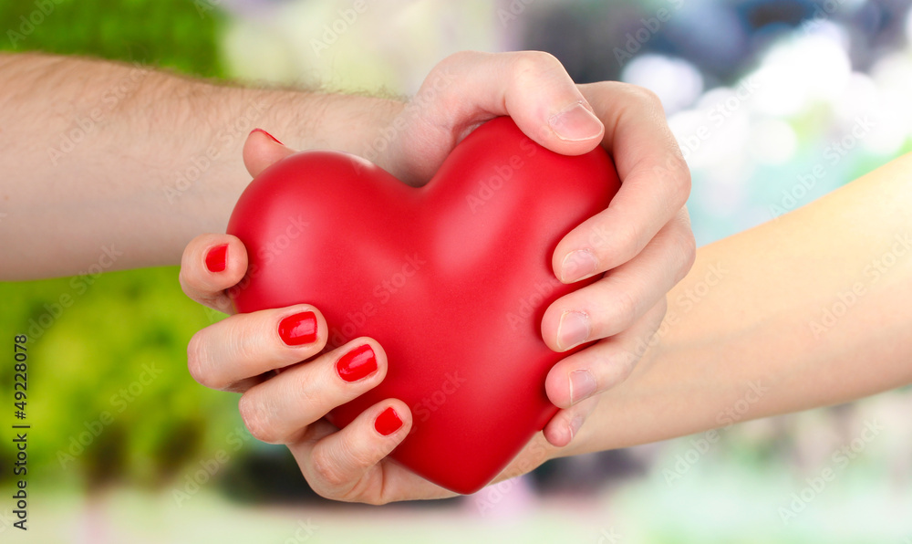 Red heart in woman and man hands, on green background Red heart in woman and man hands, on green background