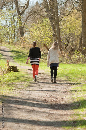 Two women walking on path in spring forest.