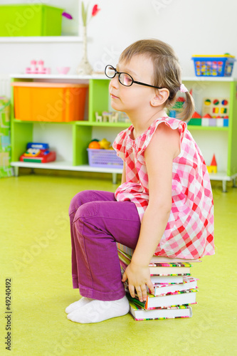 Tired little girl sitting on stack of books