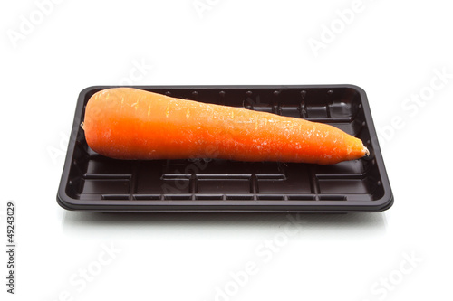 Single carrot on black plastic tray, isolated on white backgroun