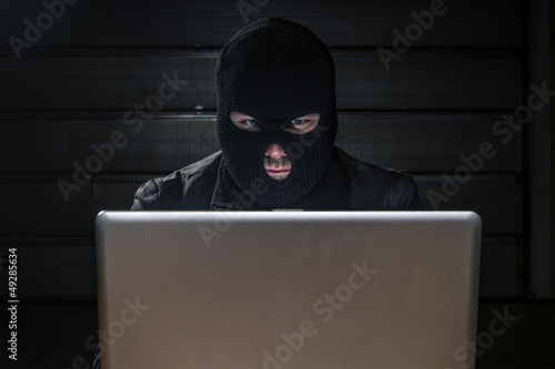 masked hacker sitting behind compuiter