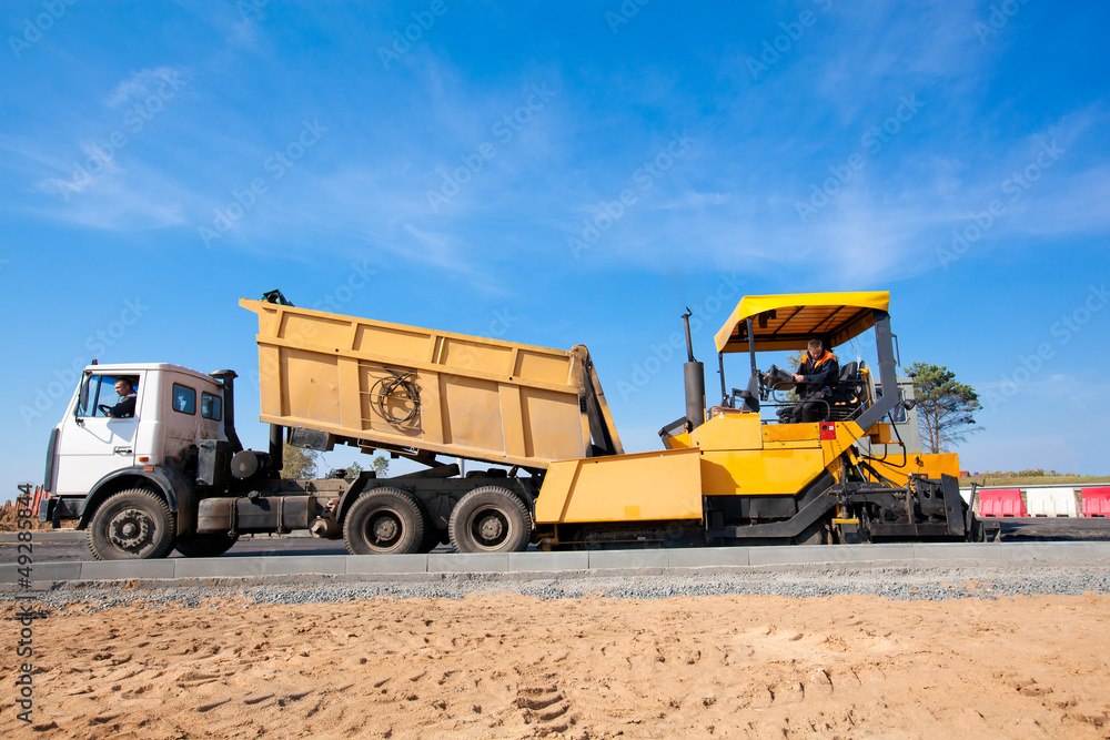 Tipper unloading fresh asphalt from body into tracked paver Tipper unloading fresh asphalt from body into tracked paver