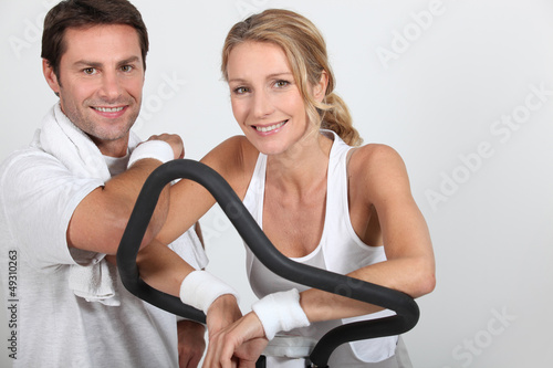 Couple wearing sportswear stood by exercise bike