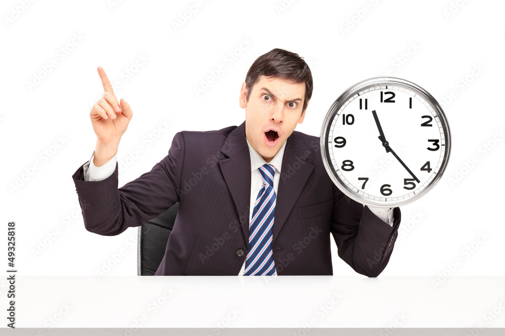 Angry businessman sitting and holding a wall clock Angry businessman sitting and holding a wall clock