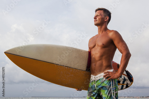 Confident professional surfer with surf board looking at ocean photo