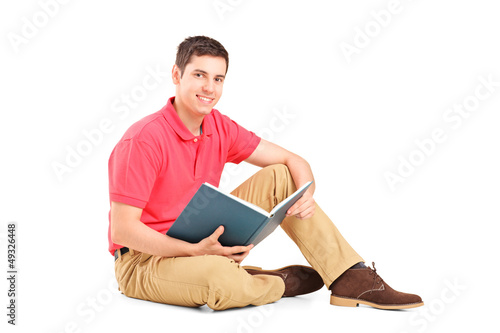 Young handsome guy sitting on a floor and reading a book