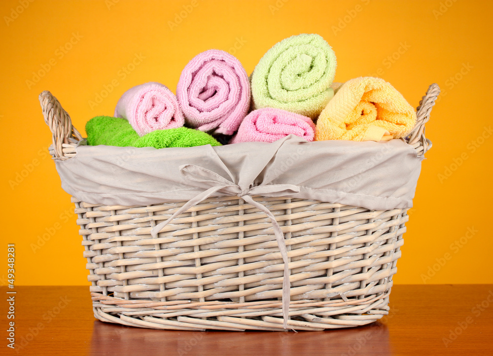 Colorful towels in basket on color background