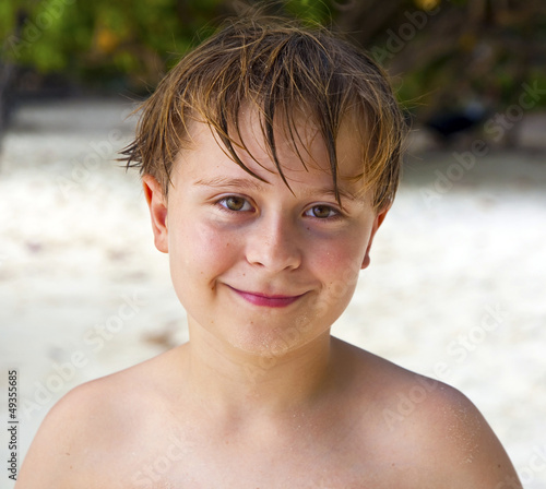 happy boy with wet hair at the beach smiles and looks very self