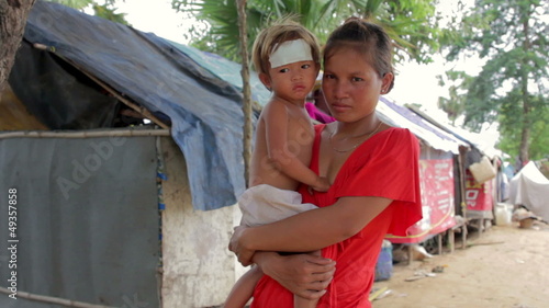 Mother holding baby in cambodian shanty, close dumping area