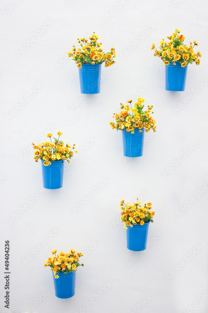 Plastic yellow flowers with metal blue vase hang in row on the w