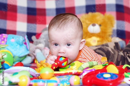 The baby lying among toys gnaws a rattle