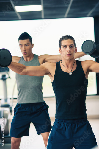 Two young men exercising with dumbbells in the gym.