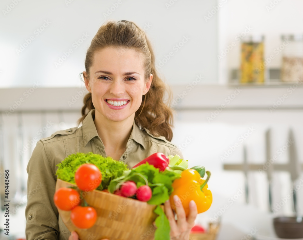Portrait of smiling young housewife showing plate of vegetables