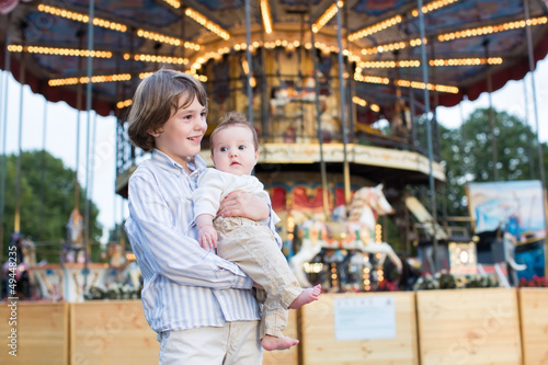 Cute boy and his baby sister standing in front of a carousel