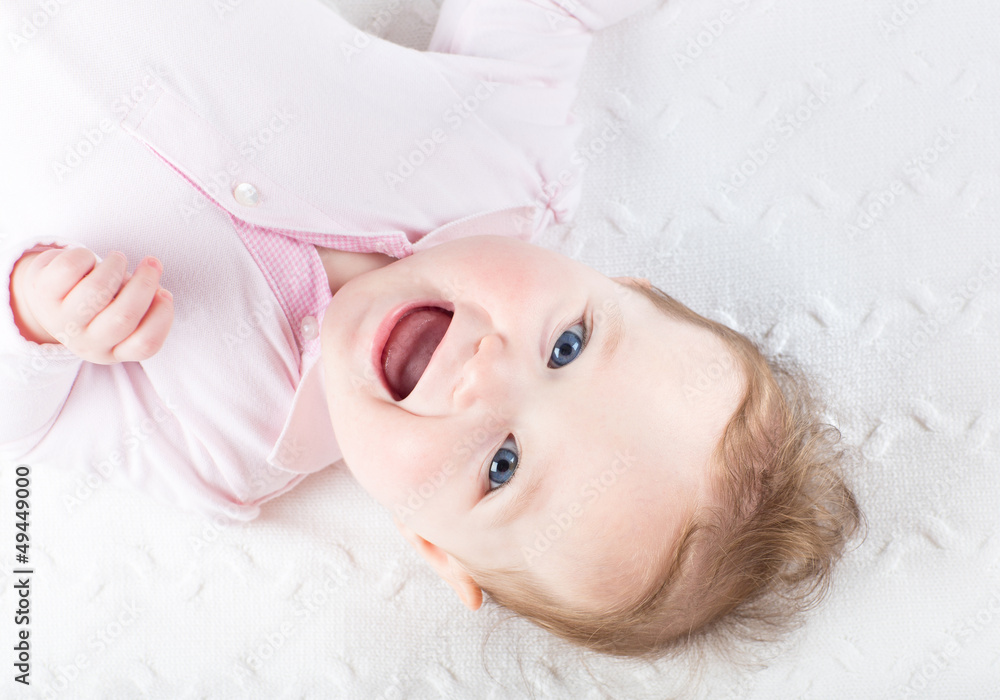 Funny laughing baby girl on a white knitted blanket