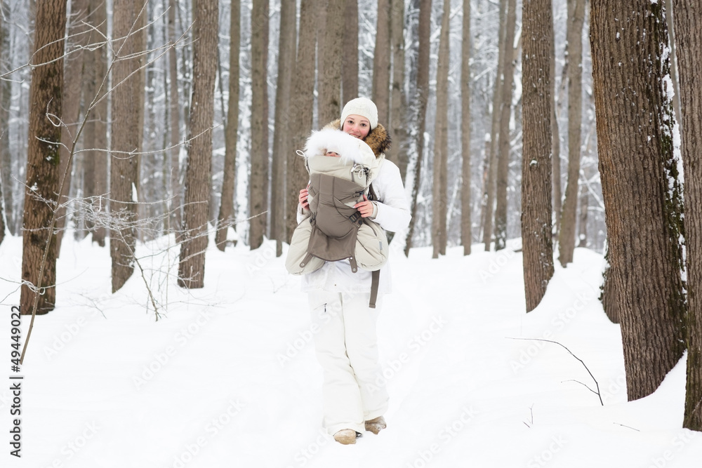 Young mother carrying baby in the forest on very snowy day