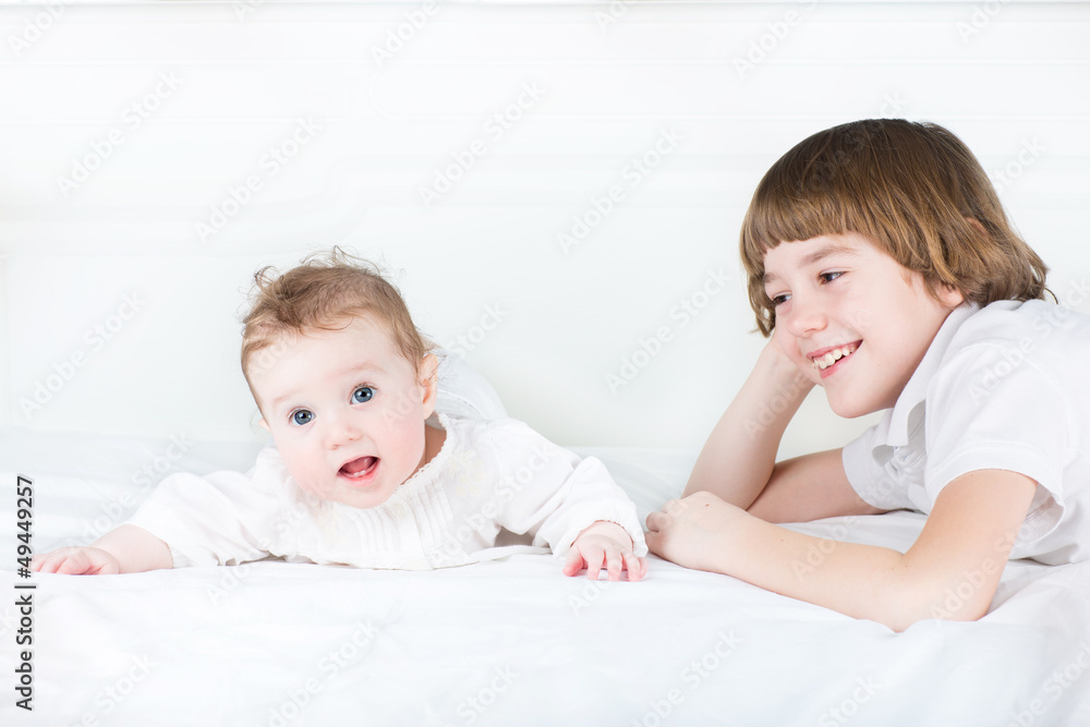 Cute boy and little sister dressed in white playing in bed Cute boy and little sister dressed in white playing in bed