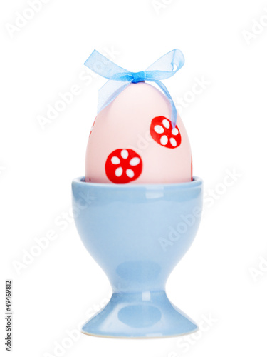 Pink colored easter egg is in blue egg cup, isolated