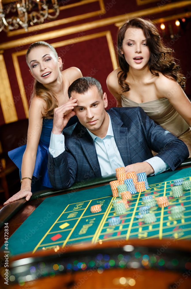 Man with two girls playing roulette at the gambling house