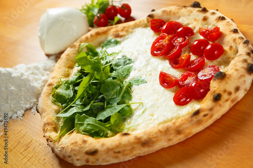 Typical Italian Pizza, ingredients in background on wood table