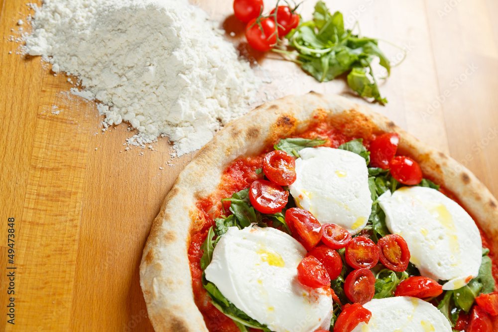 Italian Pizza with ingredients in background on a wood table Italian Pizza with ingredients in background on a wood table