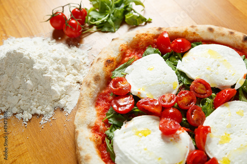 Typical Italian Pizza, ingredients in background on wood table